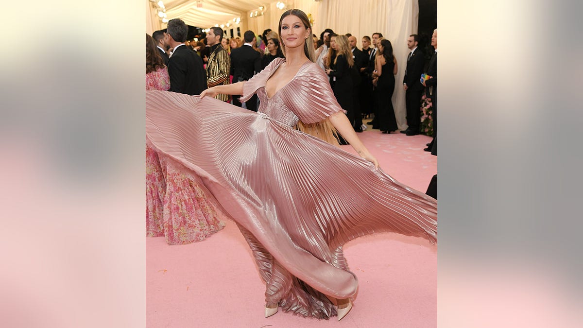 Gisele Bündchen at the 2019 Met Gala in a mauve, pink pleated silk dress twirling on the red carpet