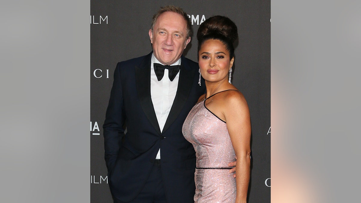 Salma Hayek in a baby pink sequin halter dress with a massive bun up-do on the red carpet with husband François Henri Pinault in a blue tuxedo