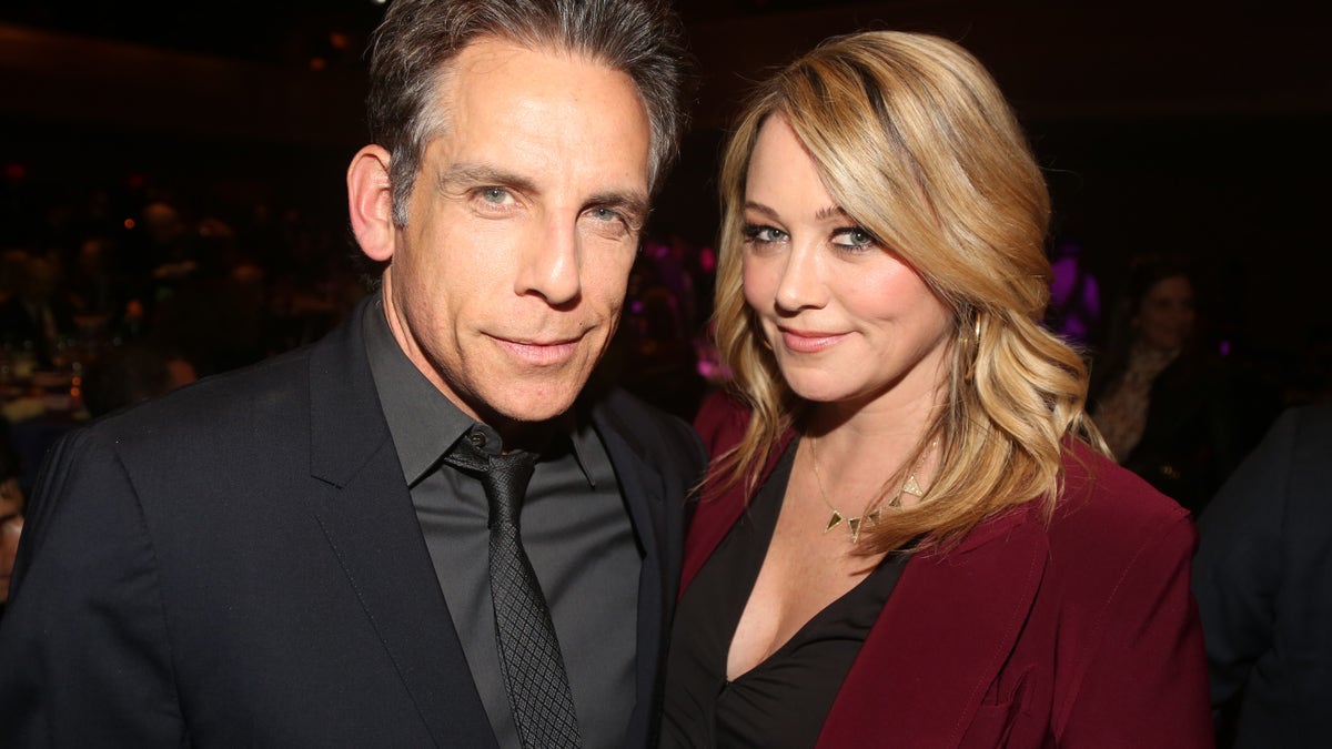 Ben Stiller in a black jacket smiles next to wife Christine Taylor in a black shirt and crimson jacket