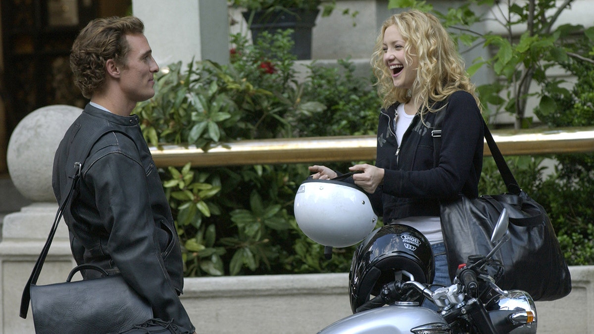 Matthew McConaughey in black playing Ben on the set of "How to Lose a Guy in 10 Days" while Kate Hudson in a white shirt and black jacket plays Andie and laughs in front of a moped