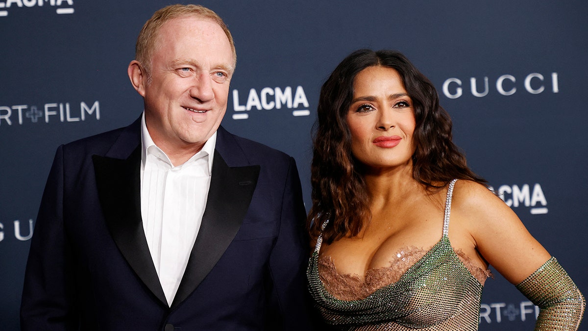 Salma Hayek in a busty mesh dress with husband François Henri Pinault in a navy tuxedo jacket and white shirt