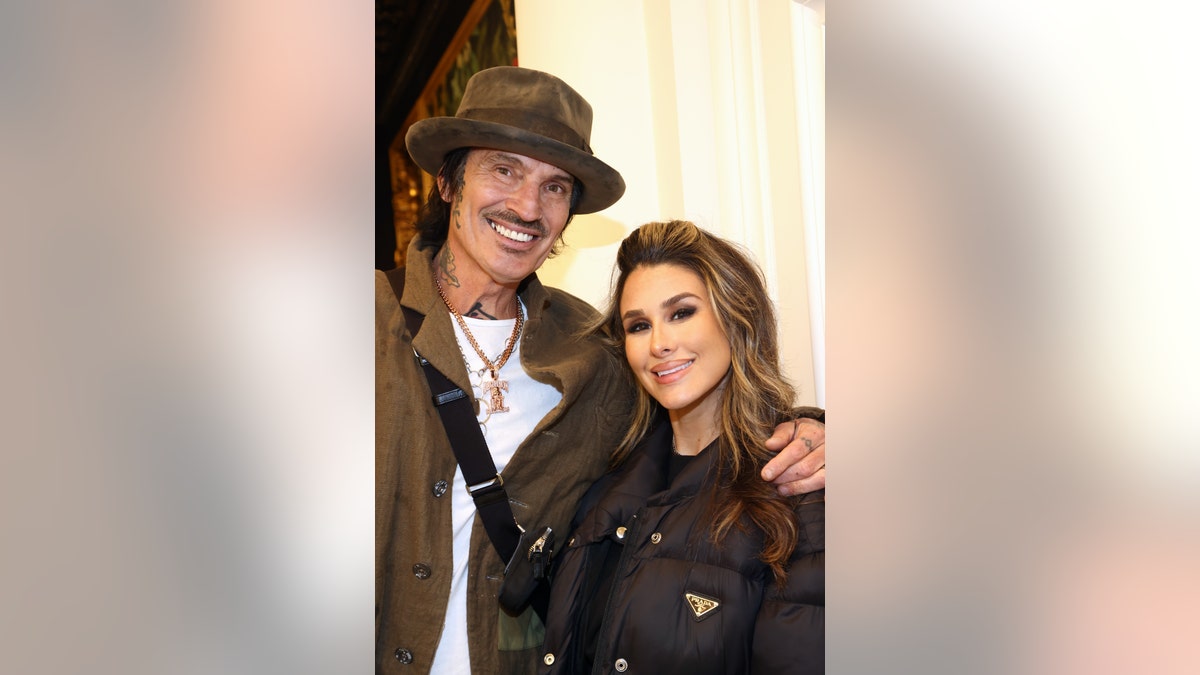 Tommy Lee wears a hat and Brittany Furlan smiles as the couple poses together