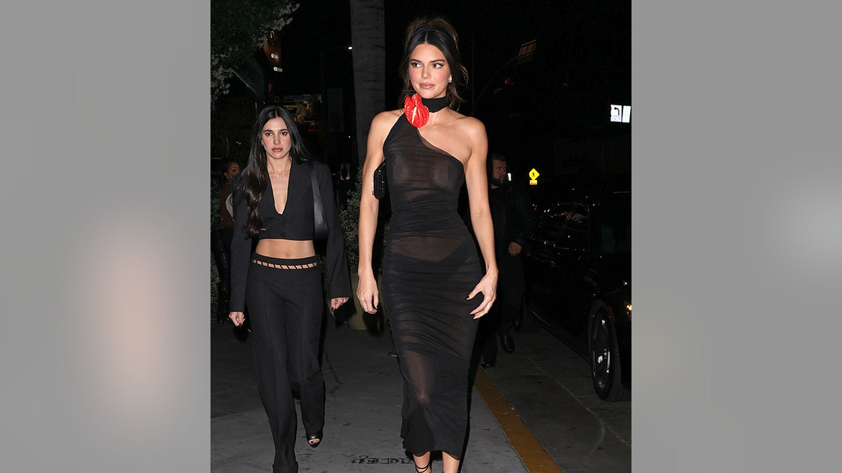 Kendall Jenner in a see-through black dress with no bra and black underwear and a red flower at the halter line of her dress