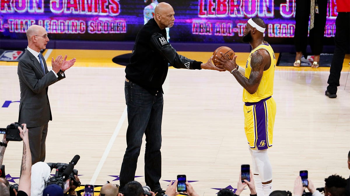 Kareem Abdul-Jabbar hands a ball to LeBron James