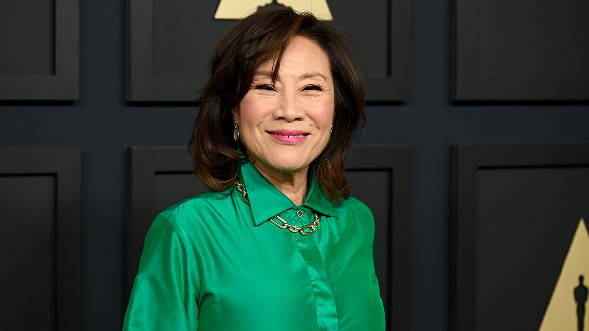 Janet Yang, the Academy's president, smiles on the red carpet in a collared long sleeve green gown at the Oscars nominee's lunch
