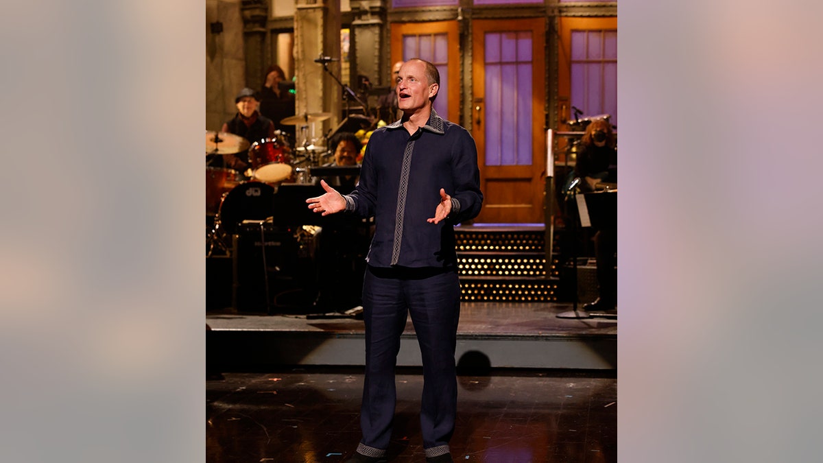 Woody Harrelson stands on stage with palms turned up like he is preaching during his opening monologue at "SNL"
