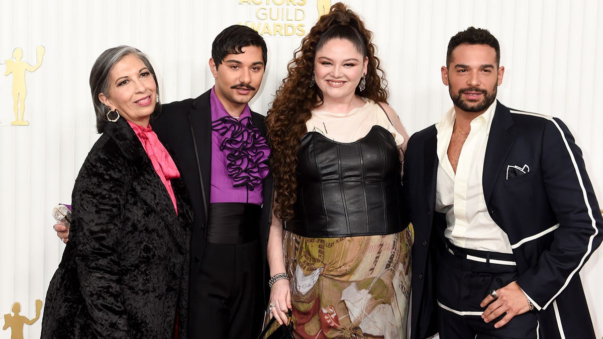Rose Abdoo in a patterned black jacket and hot-pink blouse poses next to Mark Indelicato in a purple ruffle blouse, high-waisted black pants with a cummerbund and black suit, next to Megan Stalter in a leather pleated tube top with a patterned skirt next to Johnny Sibilly in a black suit with white trim