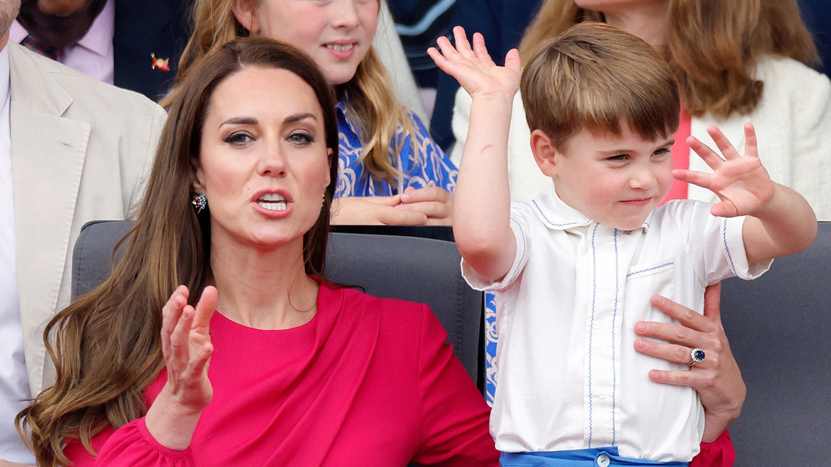 Kate Middleton in a red dress looks towards the cameras as Prince Louis' antics are caught while at an event for the Platinum Jubilee for the Queen