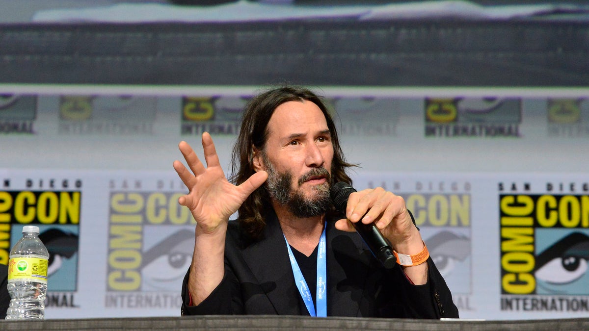 Keanu Reeves with a microphone in hand speaking at Comic-Con 2022