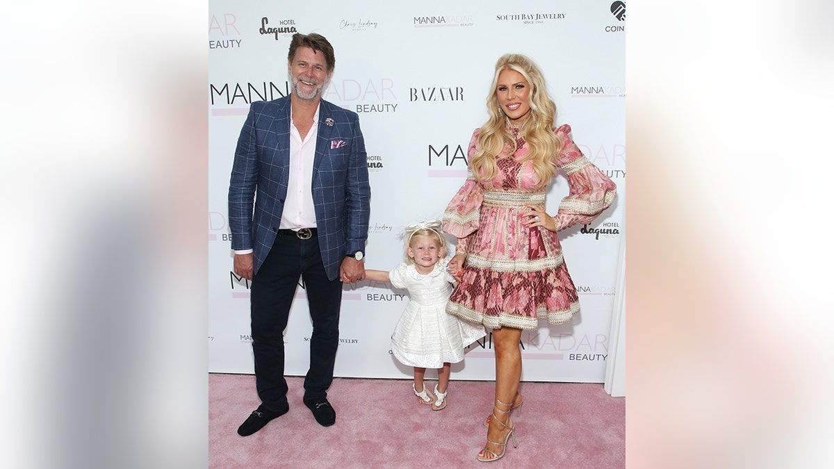 Slade Smiley in a blue jacket, white shirt, black pants holds hands with Skylar Gray in a white dress who holds hands with Gretchen Rossi in a pink lace tiered dress