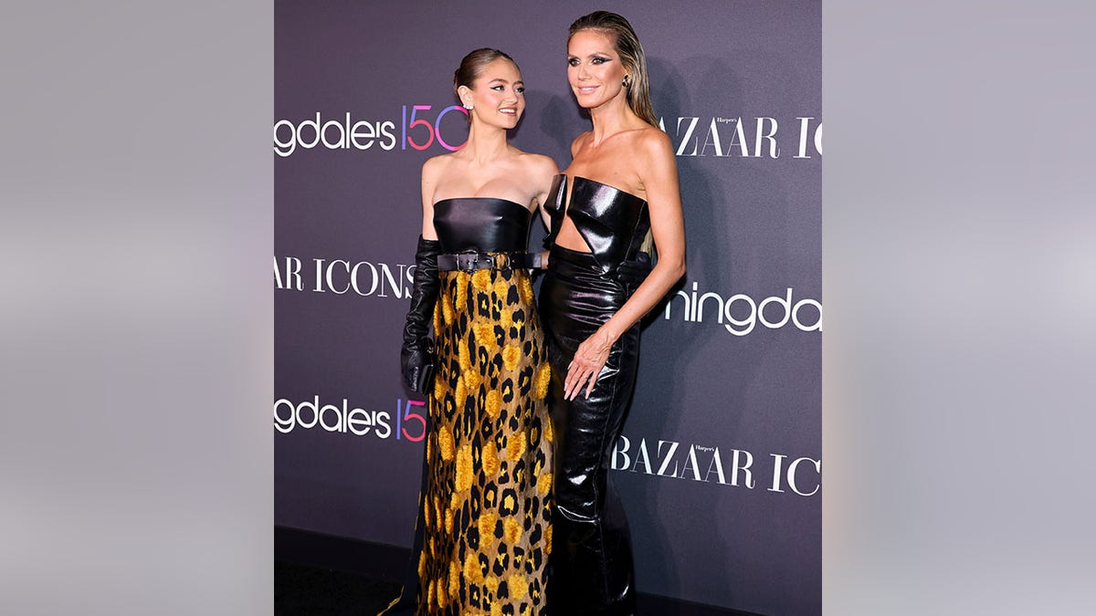Heidi Klum in a leather dress with a cut-out top poses on the carpet with daughter Leni in a patterned dress with a leather top and yellow/orange skirt and black long gloves