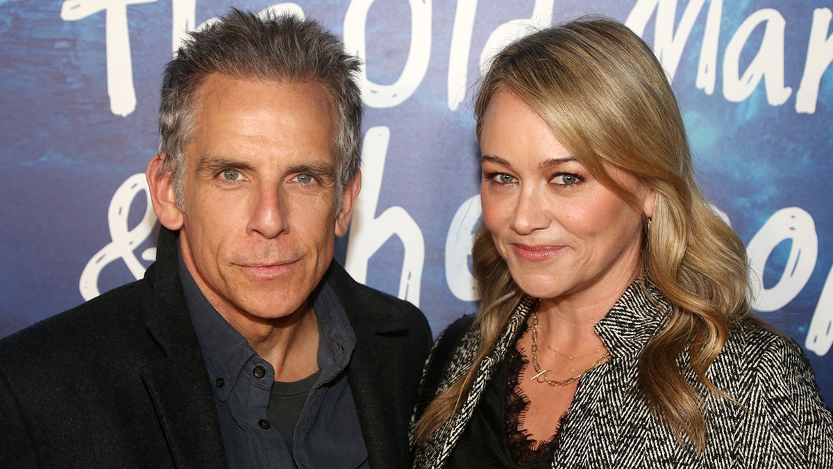 Ben Stiller wears a navy shirt and black jacket and poses for a photo with wife Christine Taylor in a black shirt and chevron jacket on the red carpet