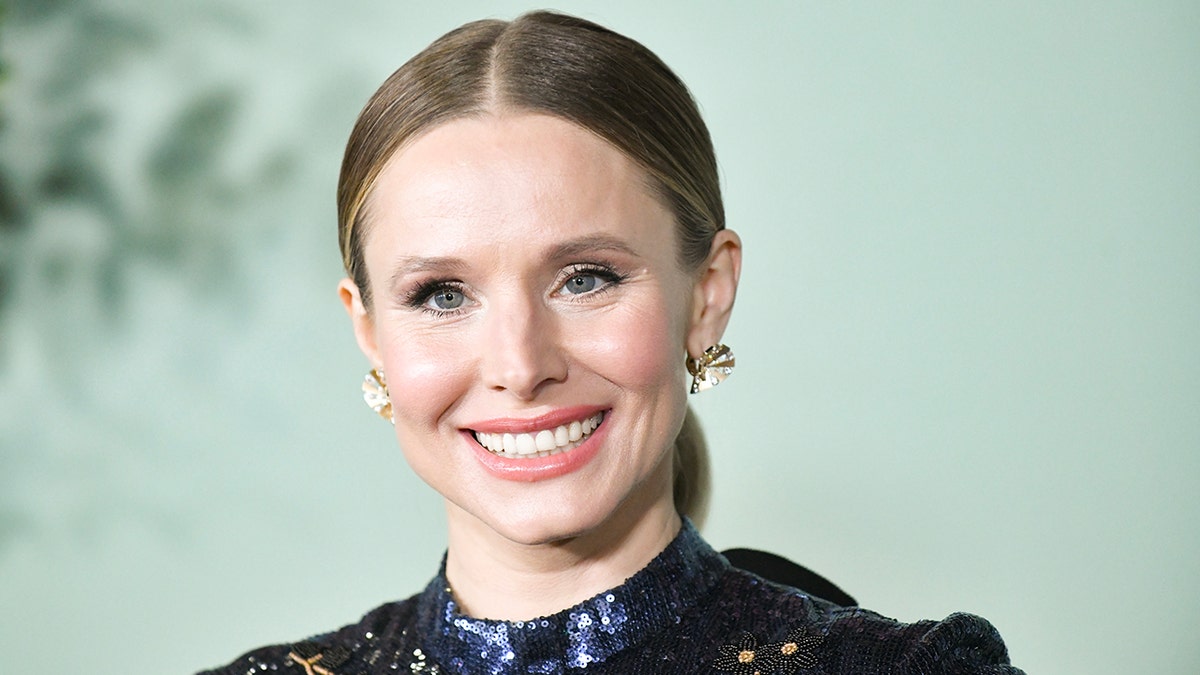 Kristen Bell with her hair pulled back in a blue sequin outfit and large statement earrings on the red carpet