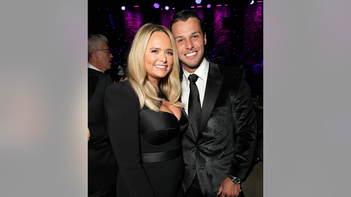 Miranda Lambert smiles next to her husband Brendan McLoughlin, both in black outfits, inside Clive Davis' Pre-Grammy Gala