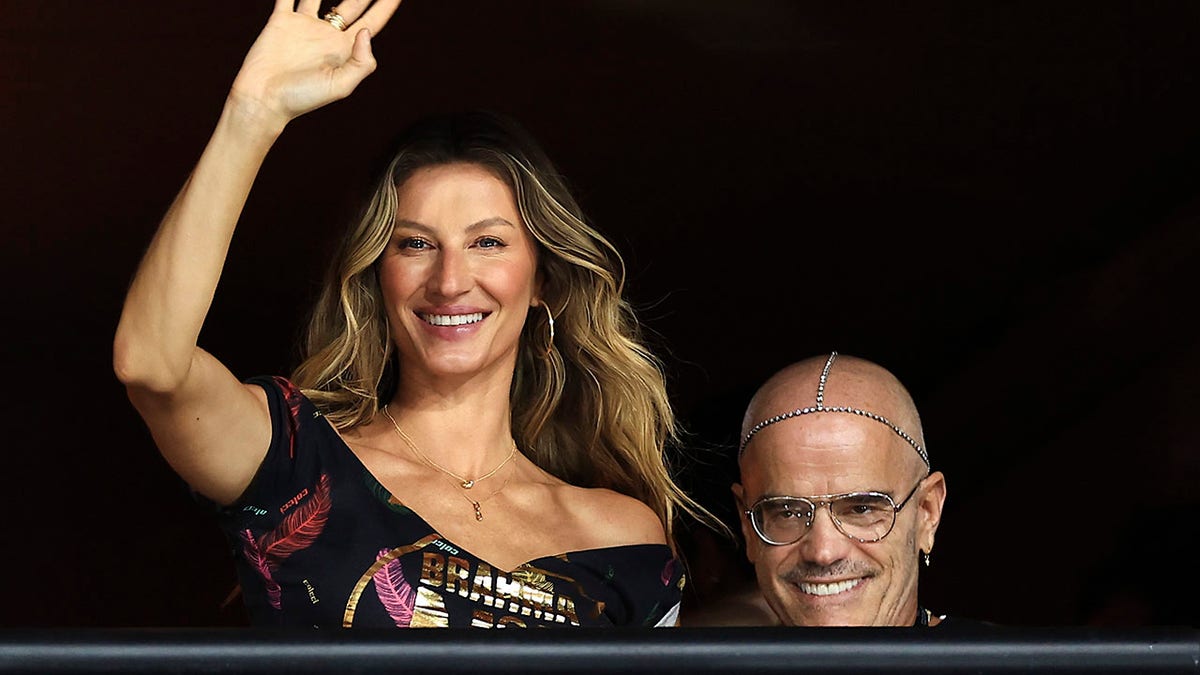 Gisele Bündchen waves at the crowd while man in glasses smiles behind her during Carnival