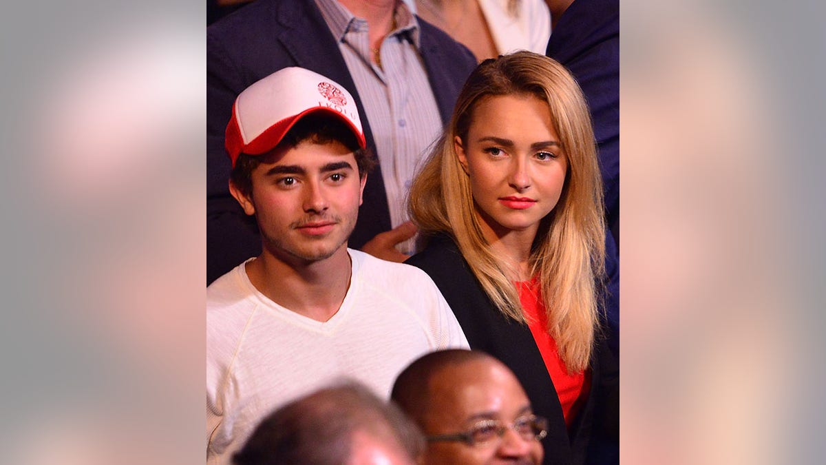 Jansen Panettiere in a white v-neck and red and white baseball hat sits next to sister Hayden in a red shirt and black jacket