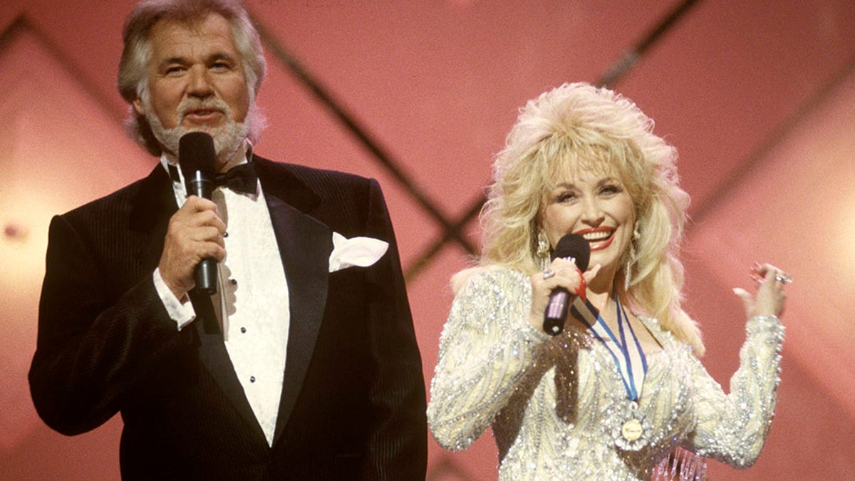Kenny Rogers in a black tuxedo and Dolly Parton in a sparkly dress with a medal around her neck performing