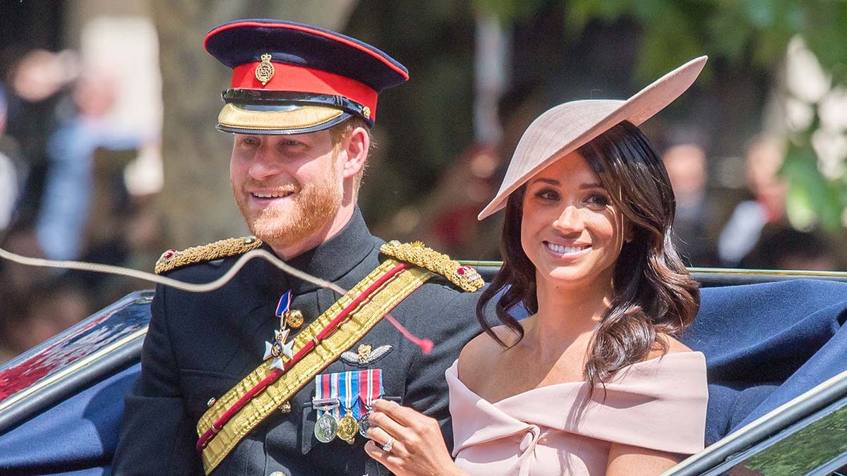 Prince Harry and Meghan Markle smile while riding in a carriage.