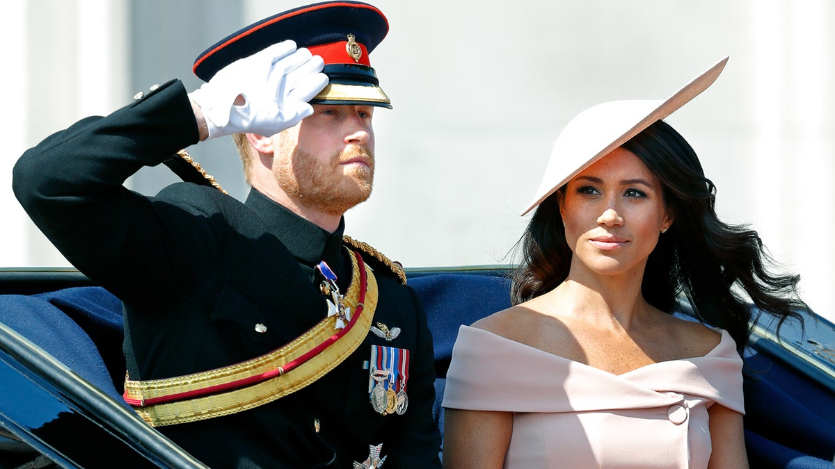 Meghan Markle wearing a powder pink suit alongside her husband Prince Harry who is in his military uniform