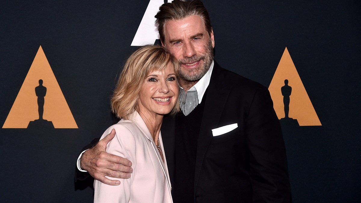 Olivia Newton-John and John Travolta smiling and embracing each other years after Grease came out