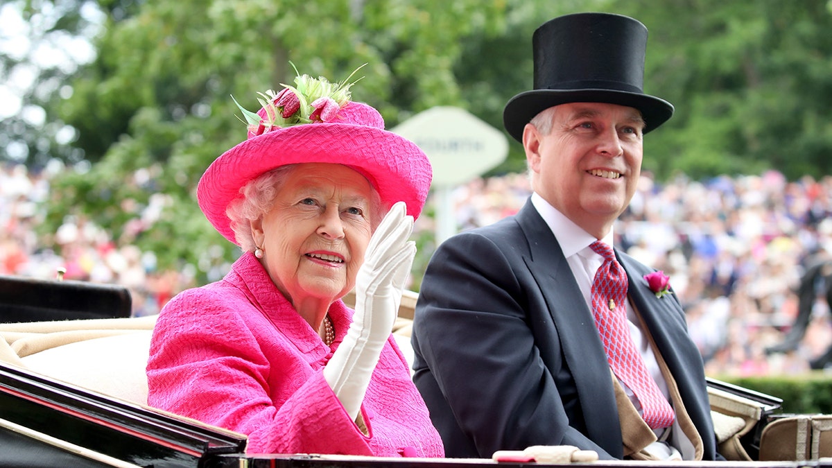 Queen Elizabeth in a pink suit waving next to her smiling son Prince Andrew in a top hat
