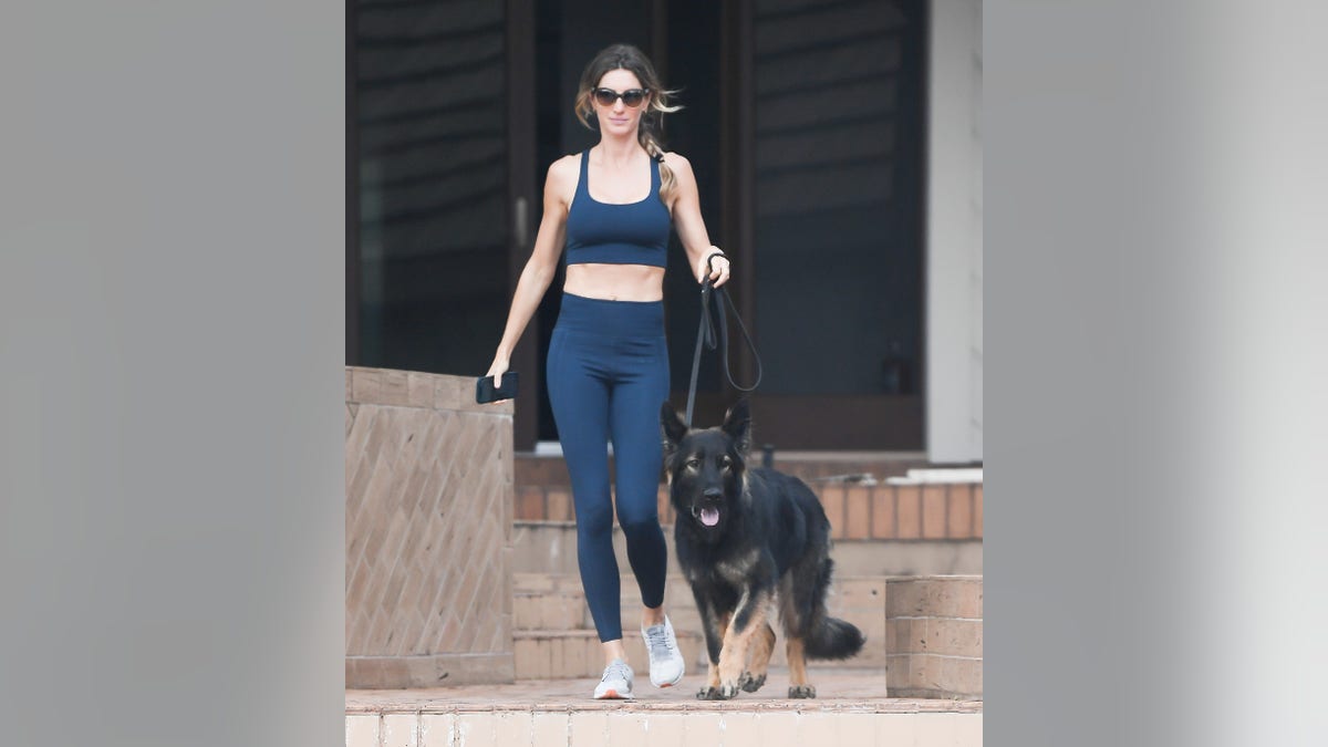 Gisele Bündchen wearing a two piece navy workout set walking a dog