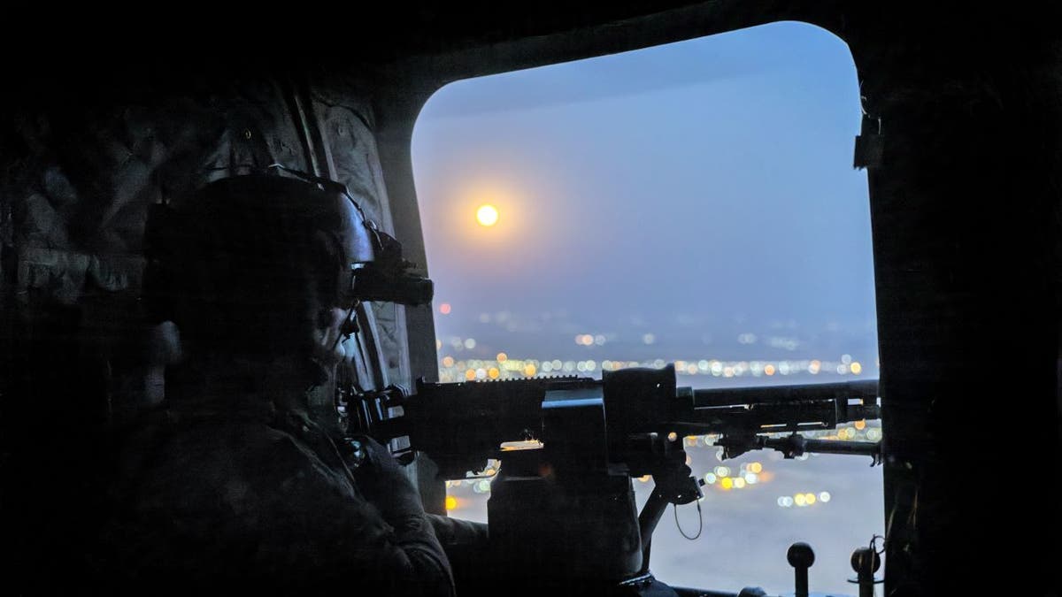 A "supermoon" shines as a U.S. Army CH-47 Chinook helicopter gunner scans the desert while transporting troops on May 26, 2021 over northeastern Syria.
