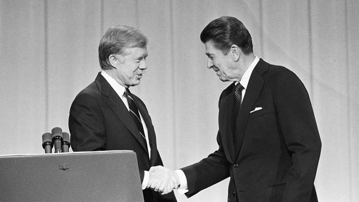 Jimmy Carter and Ronald Reagan shake hands.