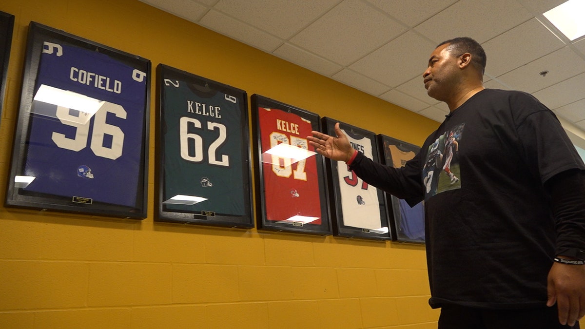 Mike Jones points to Jason and Travis Kelce jerseys mounted on the wall at Cleveland Heights High School