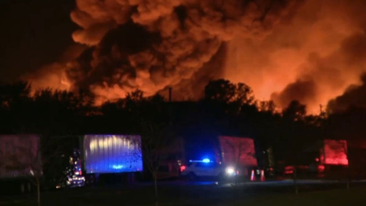 Trucks pulled over on the side of the road as a fire rages on in the background.