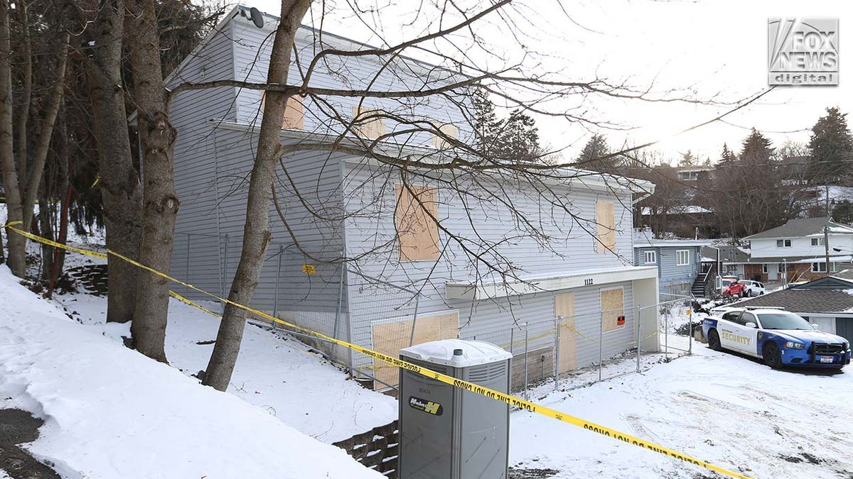 Windows on a two story house are boarded up with pieces of wood.