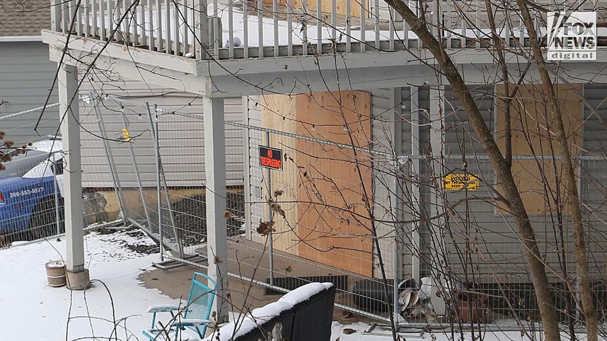 Windows on a two story house are boarded up with pieces of wood.