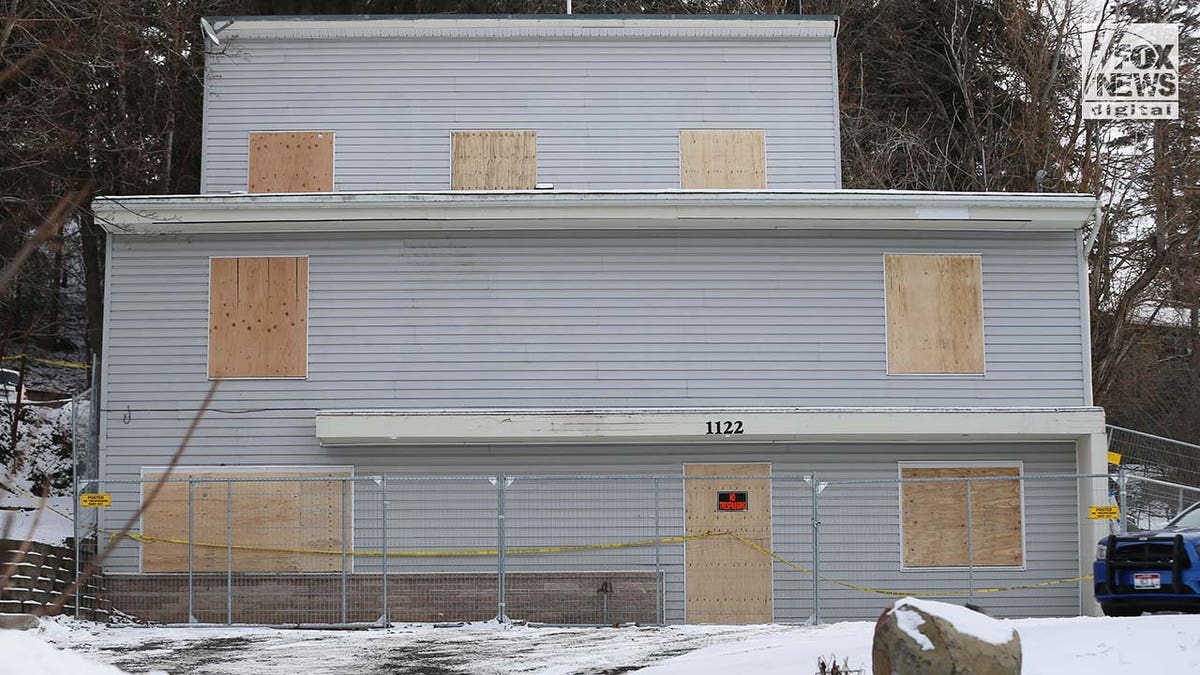 Windows on a two story house are boarded up with pieces of wood.