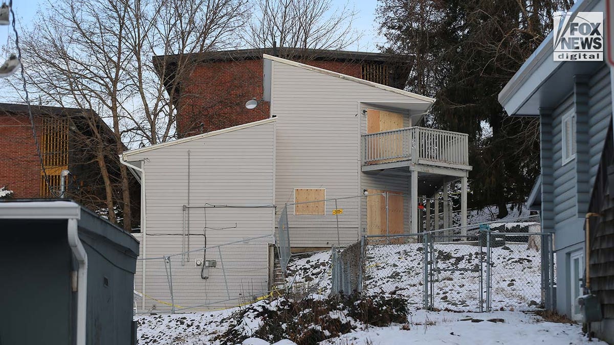 Windows on a two story house are boarded up with pieces of wood.