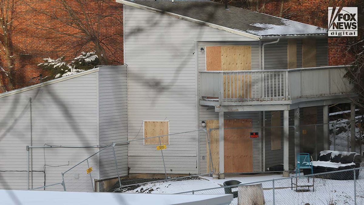 Windows to a two story house are boarded up with pieces of wood.