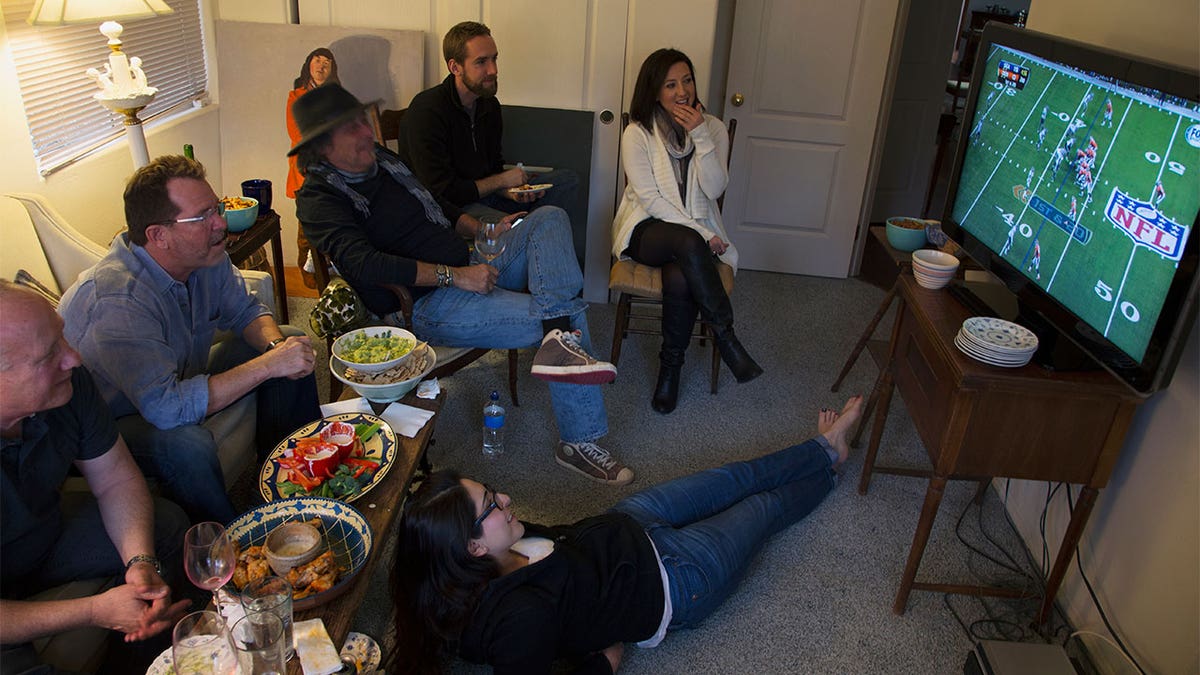 Family sitting together in the living room, sitting around the TV while watching football.