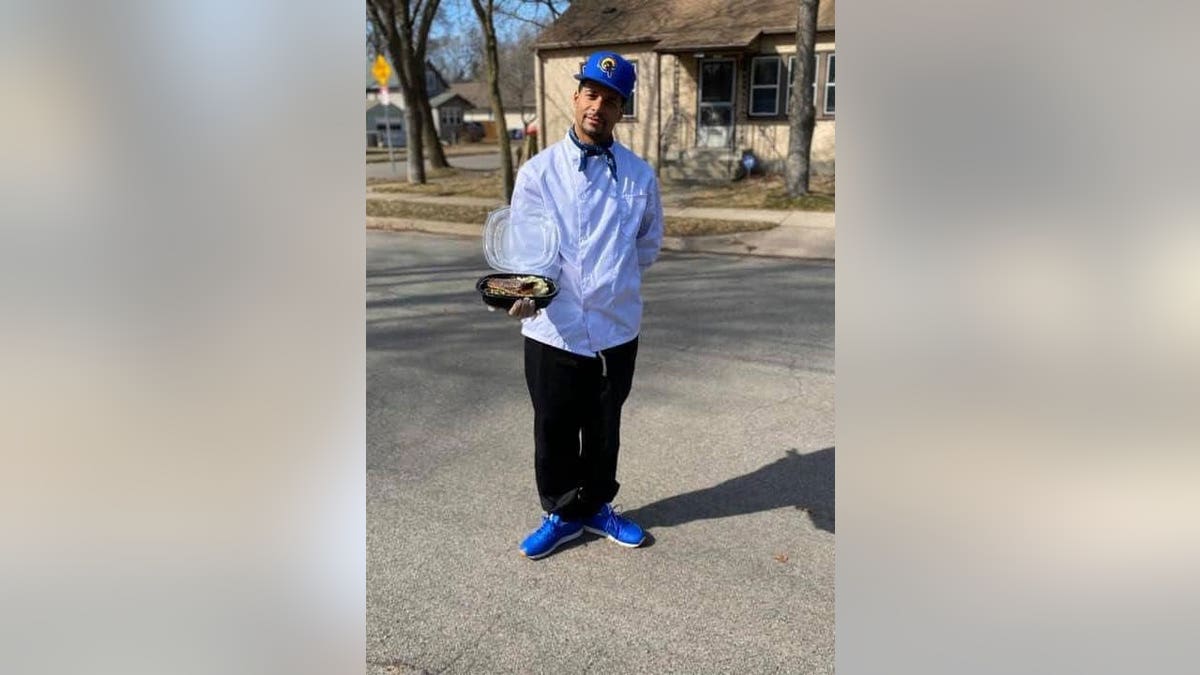 Chef standing on the street wearing a chef coat and holding a plate of food.