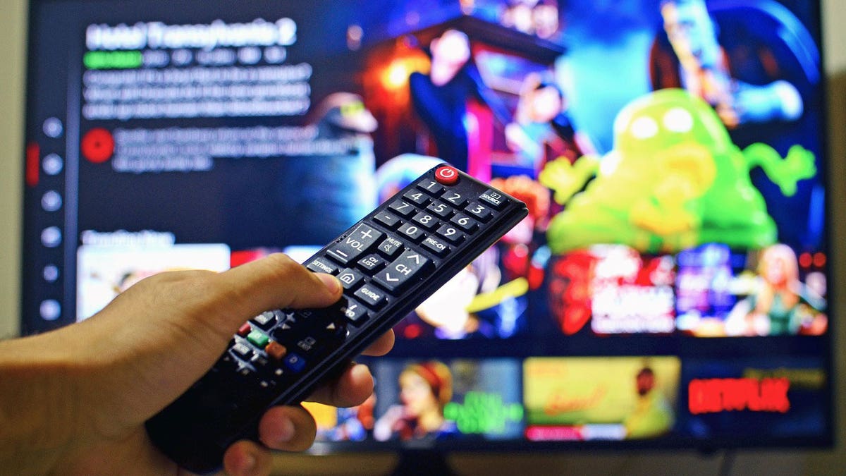 A hand holding up a remote to select something to watch on Netflix.