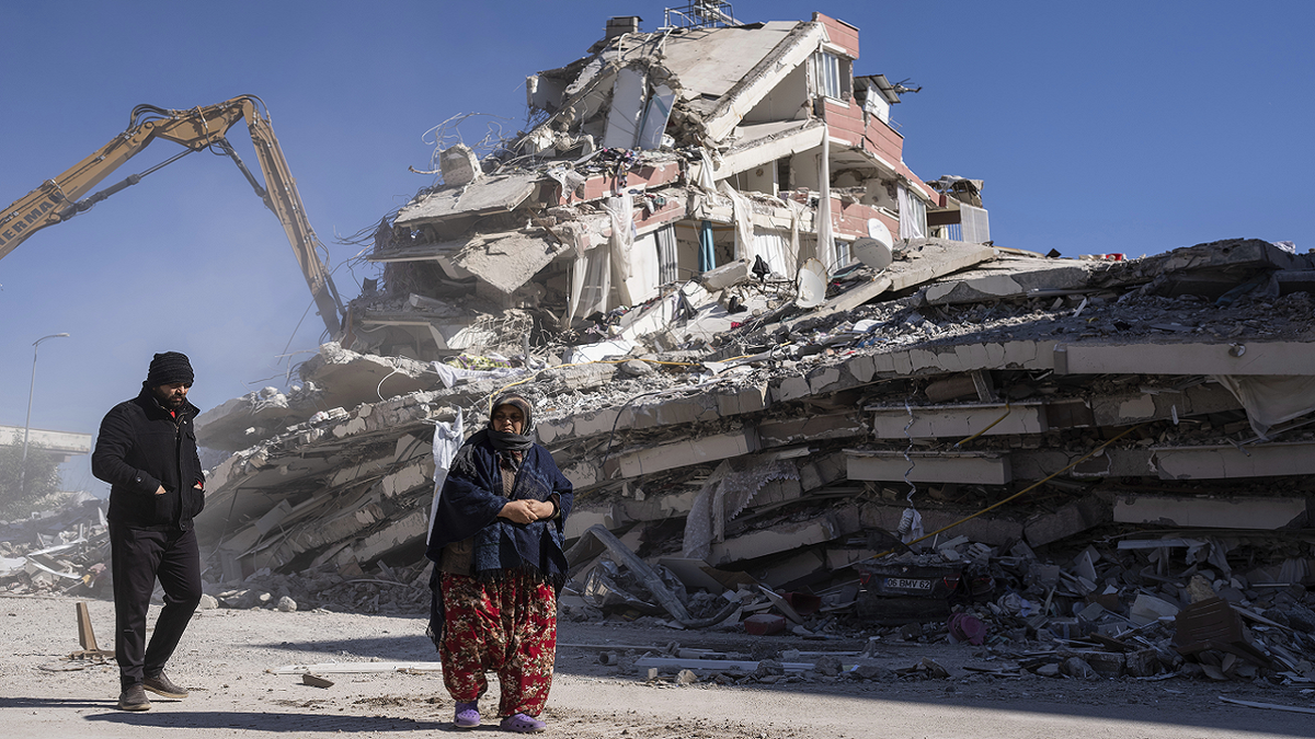 Turkish residents walk in front of building destroyed by earthquake