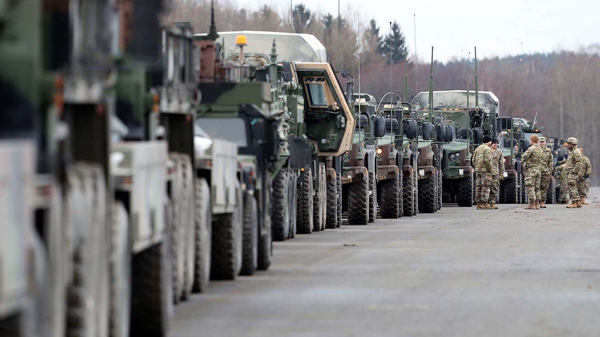 A group of soldiers stand in front of army vehicles.