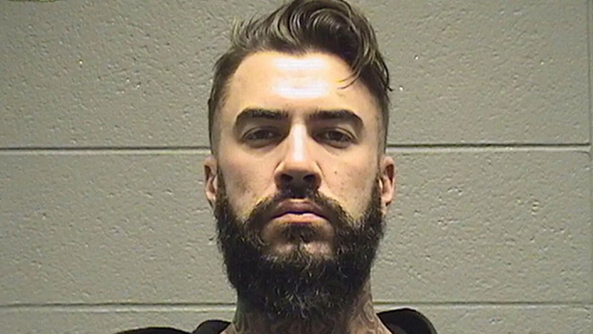 Mugshot of Connor N. Smith looking stoic in front of a white wall with a large beard and mustache