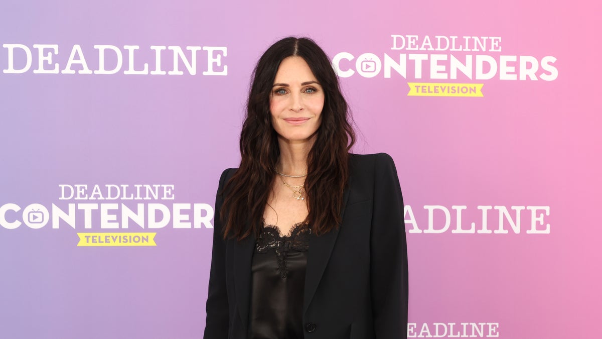Courteney Cox poses in all black on a red carpet.