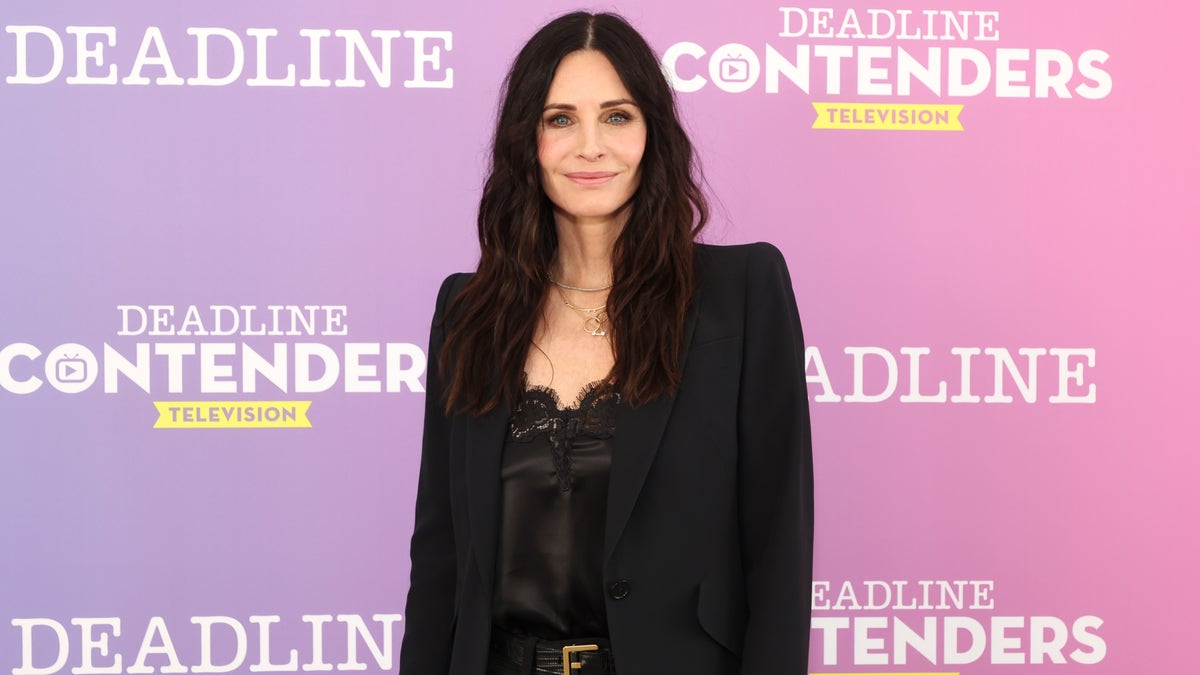 Courteney Cox poses in all black on a red carpet.