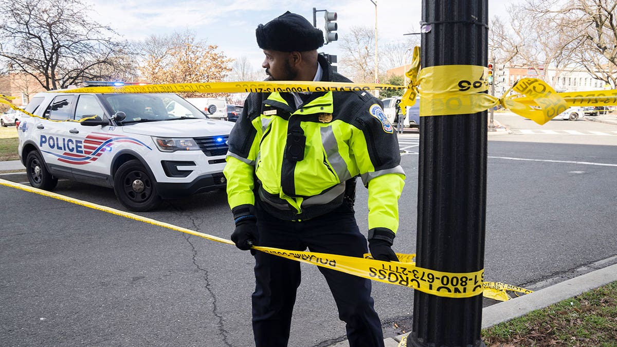 Police officer adjusts caution tape on pole