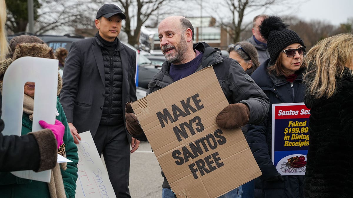 Man holds cardboard sign that says "Make NY3 Santos free" during caravan