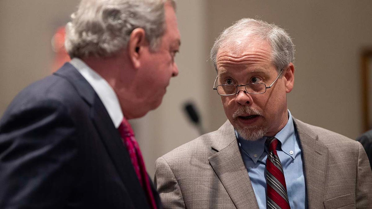 Two men speak to each other inside a courtroom.