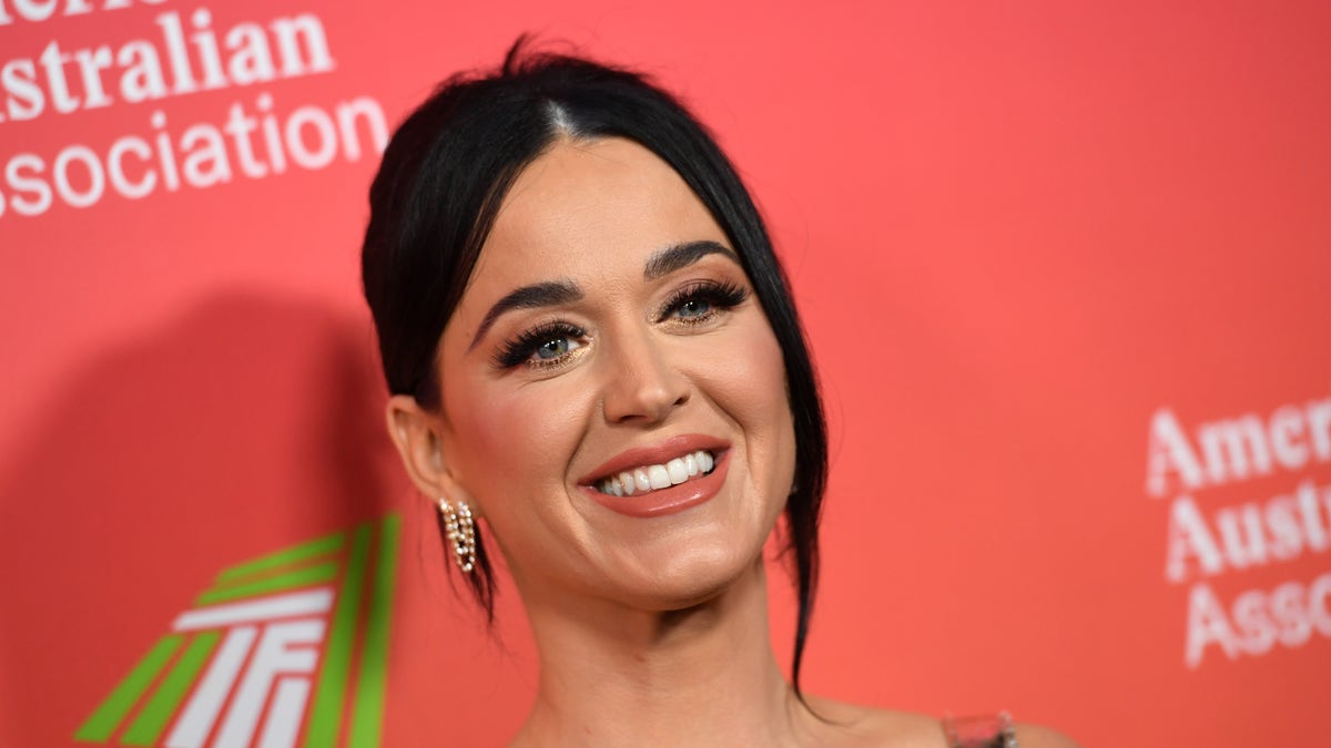 Katy Perry flashes a smile on the red carpet in a gown with her hair pulled back