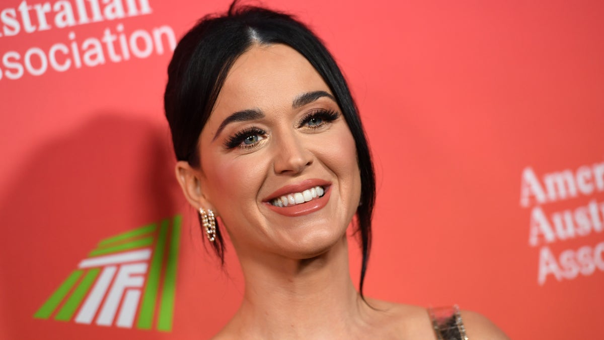 Katy Perry flashes a smile on the red carpet in a gown with her hair pulled back