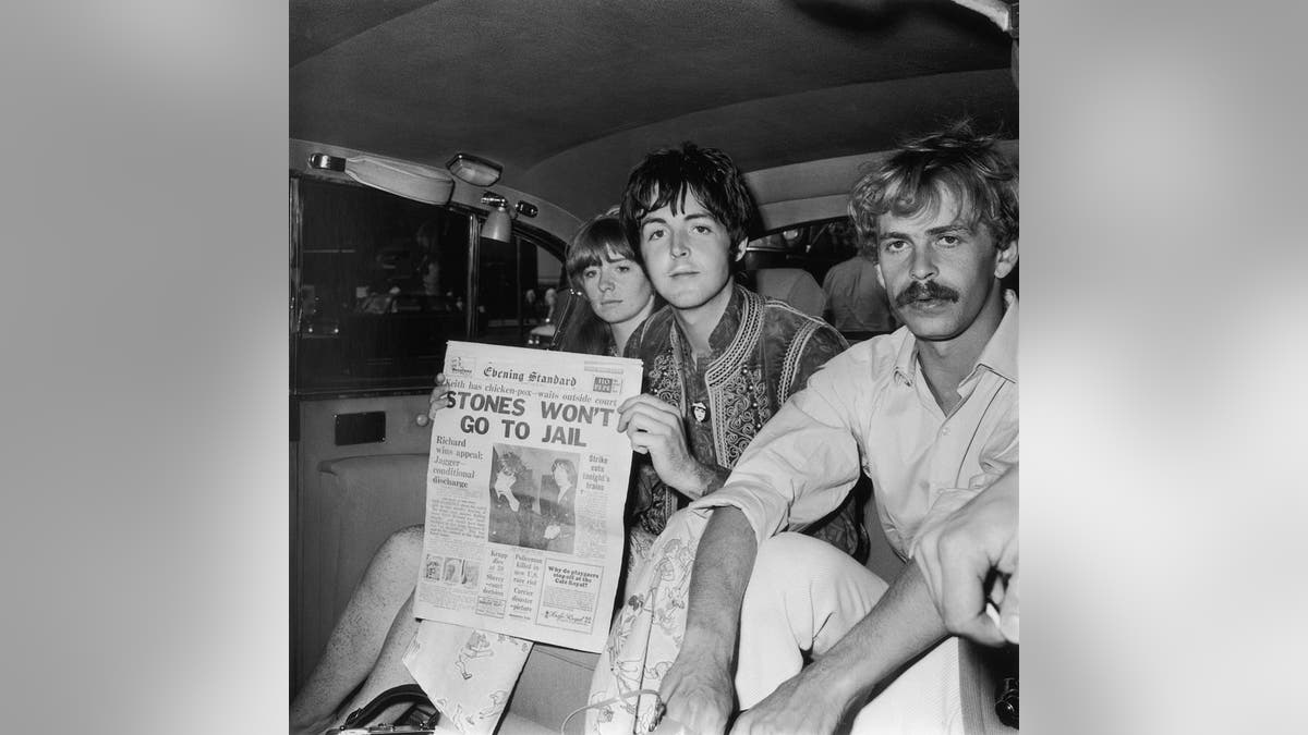Paul McCartney of the Beatles and his girlfriend, actress Jane Asher, arrive at London Airport after a trip to Greece. McCartney holds up an issue of the Evening Standard leading with a story about the drugs case involving Keith Richards and Mick Jagger and bearing the headline 'Stones Won't Go To Jail'