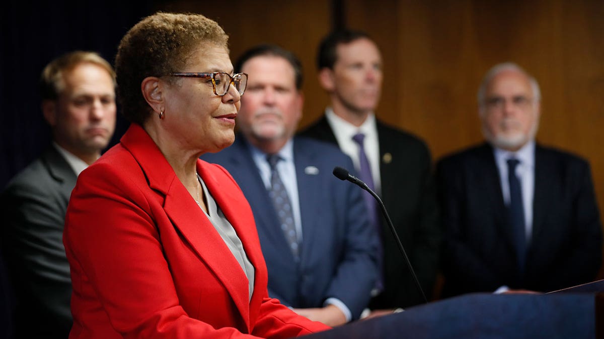 Karen Bass speaks into microphone at podium alongside LAPD